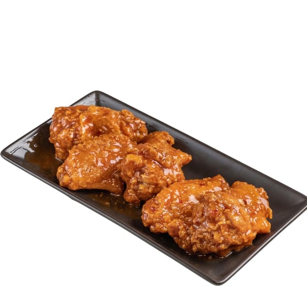 Four crispy, glazed chicken wings arranged on a rectangular black plate.