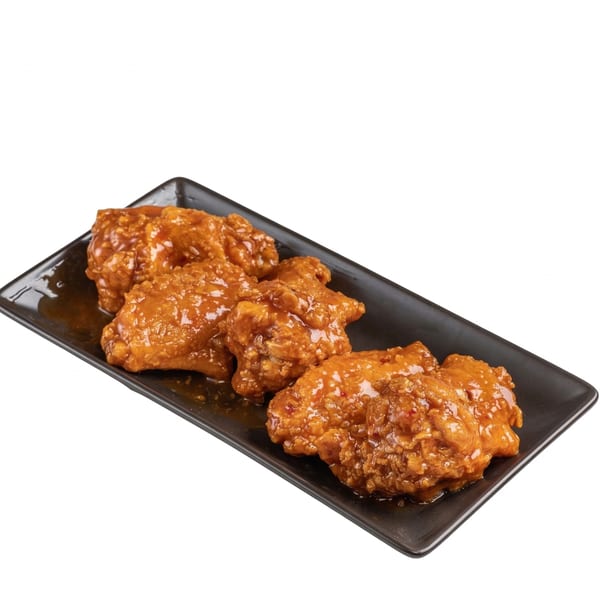 Four crispy chicken wings coated in a sweet and spicy orange glaze on a black rectangular plate.