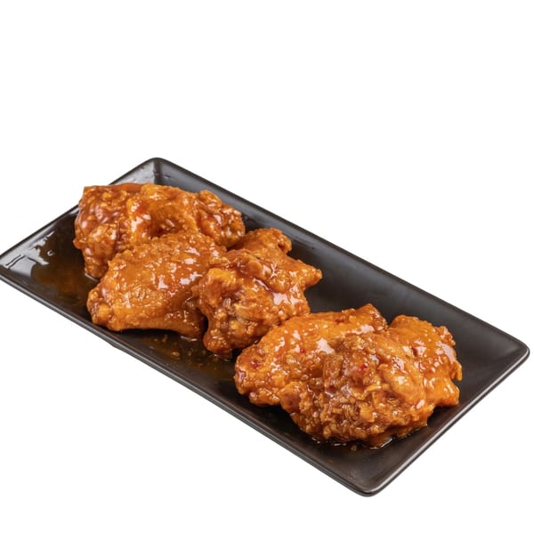 Four crispy chicken wings coated in a glistening orange sauce, served on a black rectangular plate.